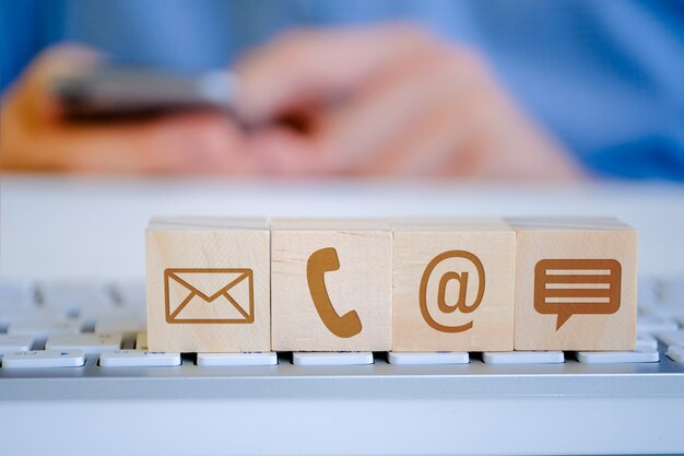 A man holds a smartphone with his hands, in the foreground there are wooden cubes with letters, email, phone and message icons. The  of viewing content.