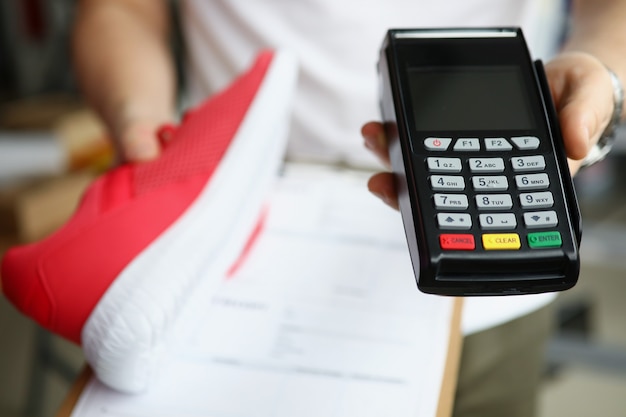 Man holds sneakers and payment terminal concept in his hands