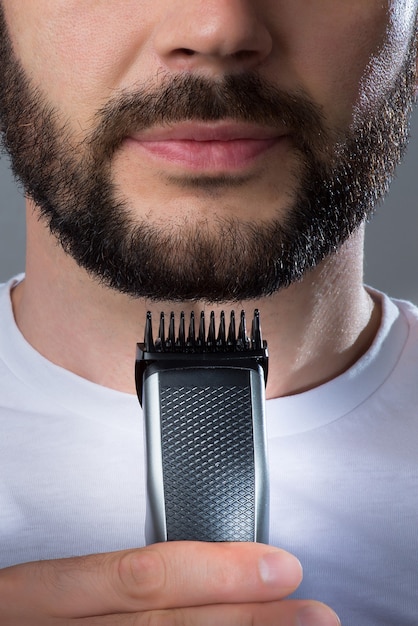 A man holds a trimer near his beard