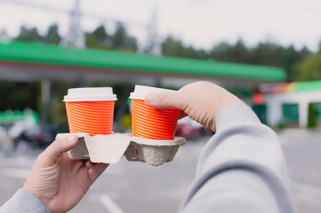 A man holds two cups of coffee in his hands at a gas station