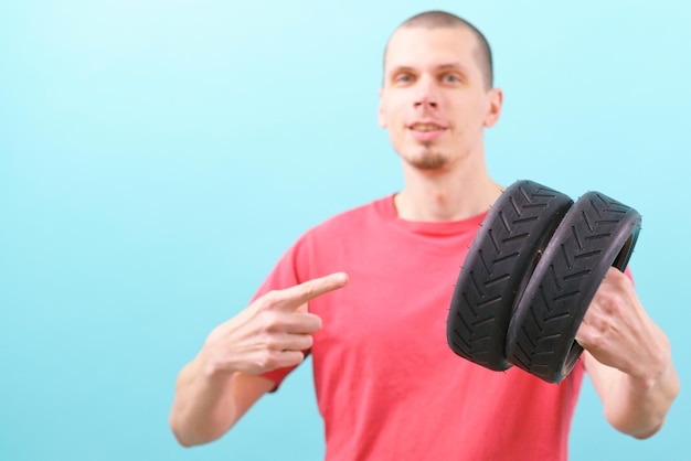 A man holds two small scooter tires and pointing his finger on\
it on a blue background wheel rubber black transportation vehicle\
tyre part repair good excellent fix fixed