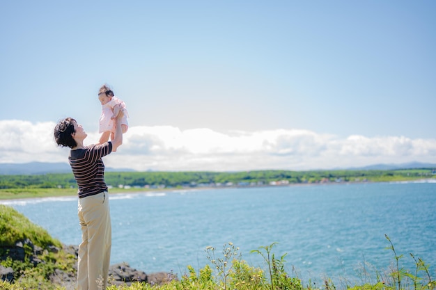 A man holds up a baby in front of a body of water.