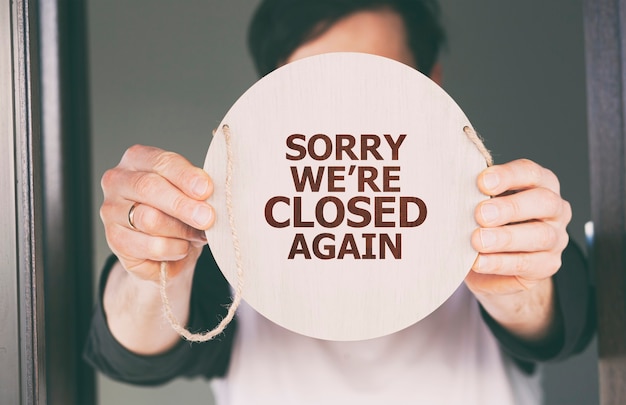 Man holds the wooden sign with text: Closed