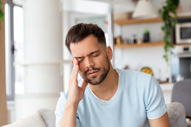 Photo man at home having a headache young man suffering from headache after hard working day sitting on couch at home