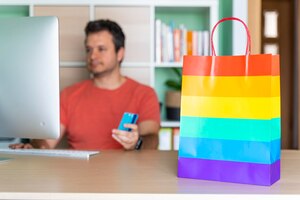 Man at home office shopping online with rainbow bag on table