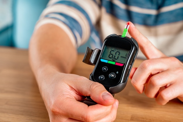 A man at home uses a glucose meter to measure blood glucose Piercing a finger with a needle