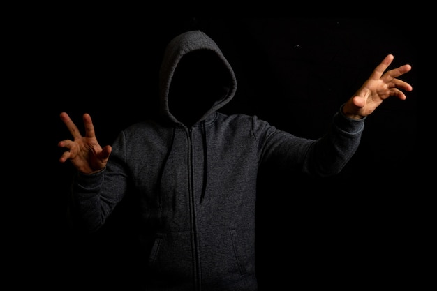 Man in a hood is touching something on a dark background.