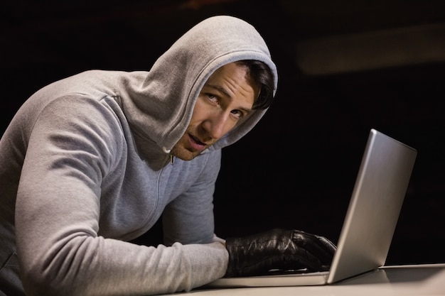 Man in hood jacket hacking a laptop while looking at camera