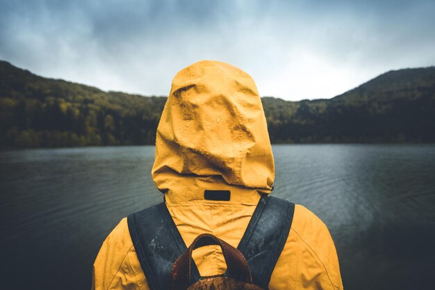 Foto uomo con il cappuccio che guarda il lago contro il cielo