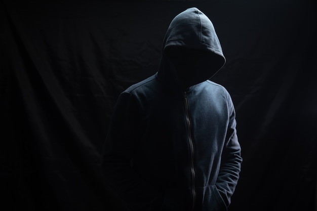フードをかぶった男性が黒い背景に立っています