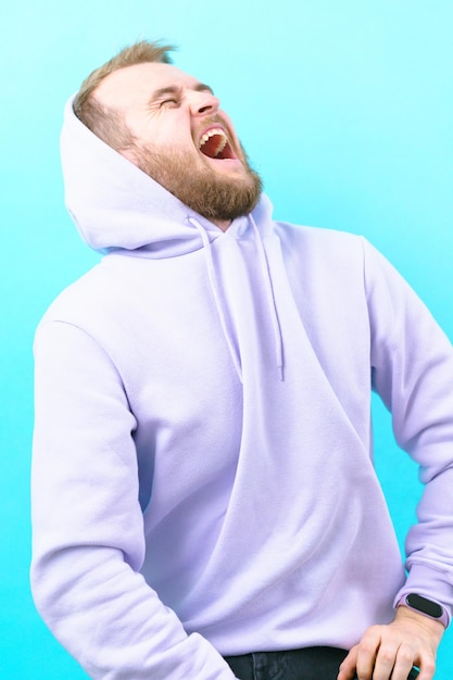 A man in a hoodie is sitting at the studio and looking up and screaming on the blue background Mouth Handsome Mental Bizarre Psycho Scream Yell Panic Noise Loud Noisy Gorgeous Teeth