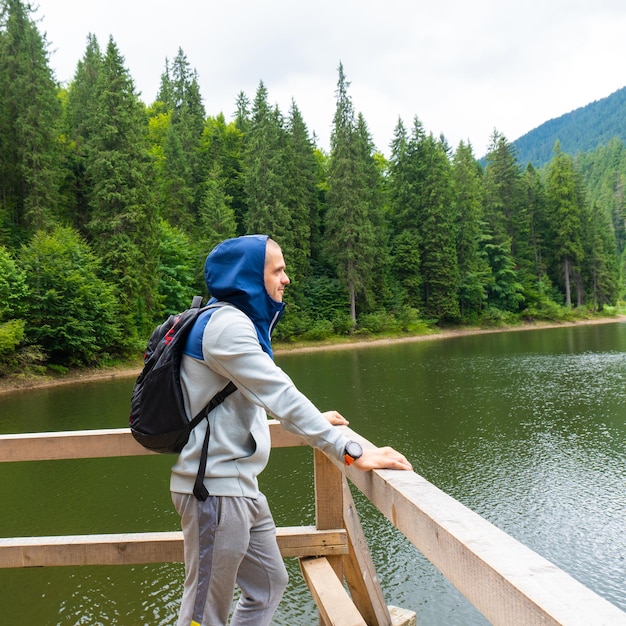 Man in hoodie with backpack looking on mountain lake. Traveller got destination