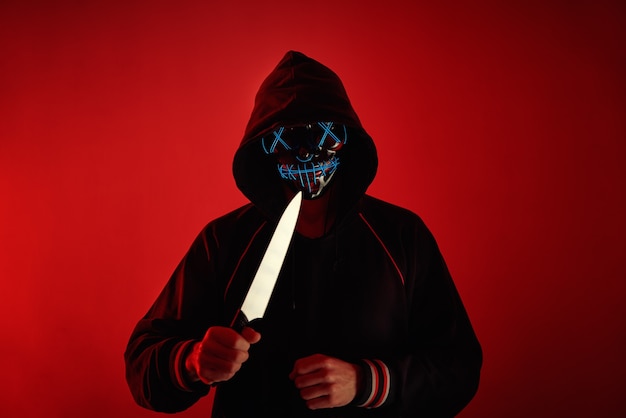 Man in hoodie with scary mask on face holds knife in hand