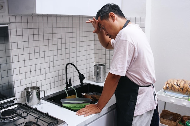 Мужчина безнадежно смотрит на кучу грязной посуды на кухне