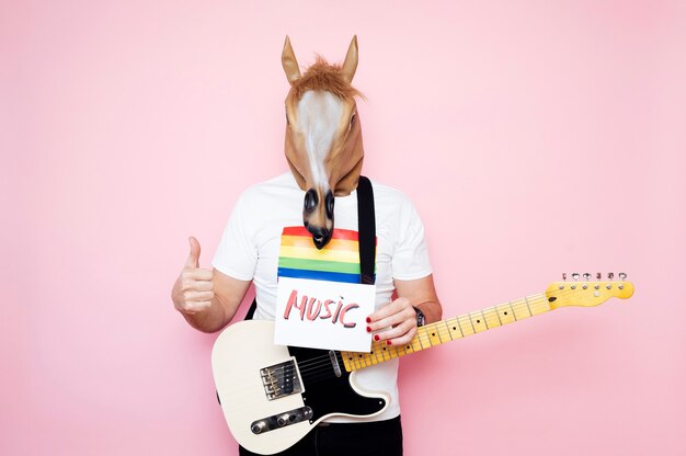 man in horse mask with thumb up holding a sign that says ¨music¨