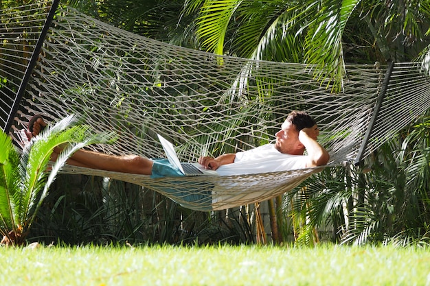 Man in a hotel in the summer with a laptop lying in a hammock