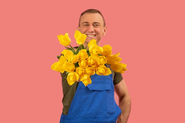 Man houdt boeket van gele tulp bloemen en glimlacht Studio portret geïsoleerd op roze achtergrond Bloemen Levering