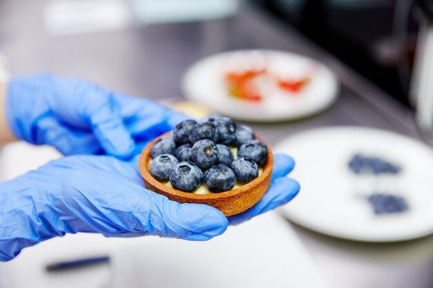 Man houdt een kom van bosbessen in handen met blauwe handschoenen