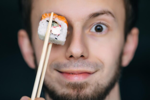 Man houdt een stuk sushirol voor zijn oog Sushi levert