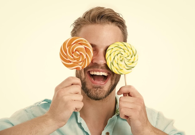 Man houdt grote lolly's op ogen als bril Zoete tand concept Guy op lachend gezicht houdt twee gigantische kleurrijke lolly's in handen geïsoleerd op witte achtergrond Man met haren houdt van snoep