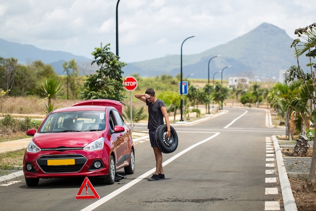 man houdt het reservewiel tegen een kapotte auto op de achtergrond van bergen en palmbomen