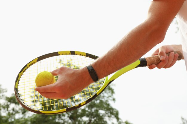 Man houdt racket en tennisbal tegen hemel