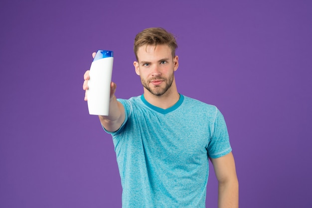 Man houdt shampoofles op violette achtergrond. Bebaarde man met gel tube op paarse achtergrond. Huidverzorging en haarverzorging. Gezondheid en gezondheidszorg. Cosmetisch voor spa en bad of douche.