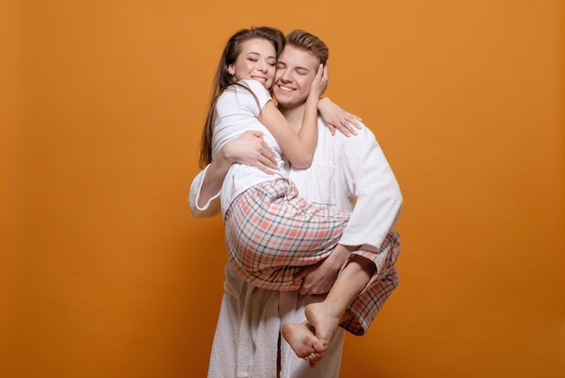 Man houdt vrouw in zijn handen, echtpaar in huis kleding op gele achtergrond, gelukkige relatie, jonge vrouw knuffels man