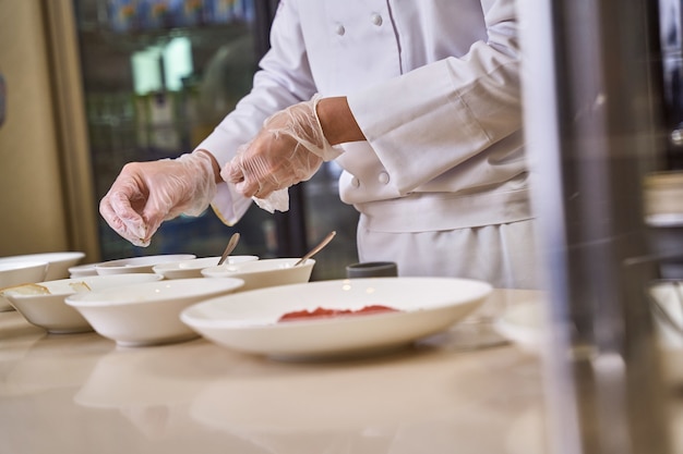 Man houdt zijn hand boven een paar diepe borden met eten en gooit een snufje kruiden en specerijen naar gerechten