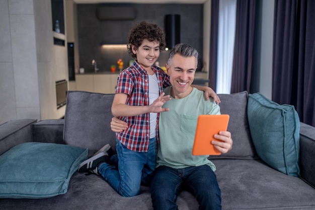 Man hugging boy smiling at tablet