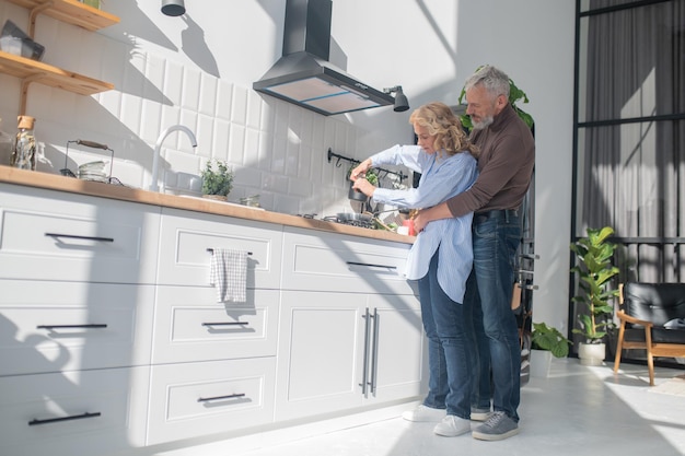 Man hugging his wife while she cooking breakfast