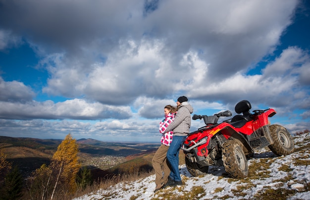 Equipaggi abbracciare una donna vicino al quad rosso su un pendio di montagna sotto il cielo blu