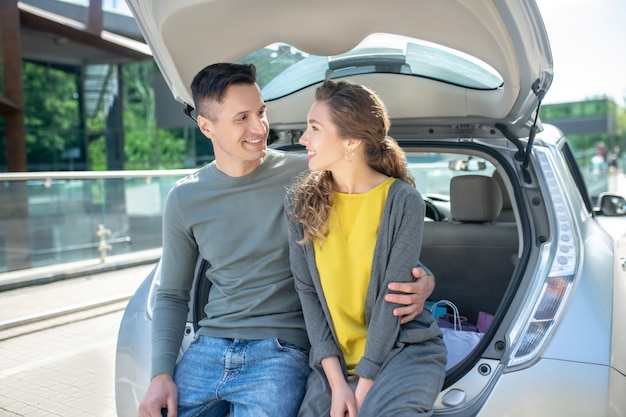 Man hugging a woman seated on an open car trunk