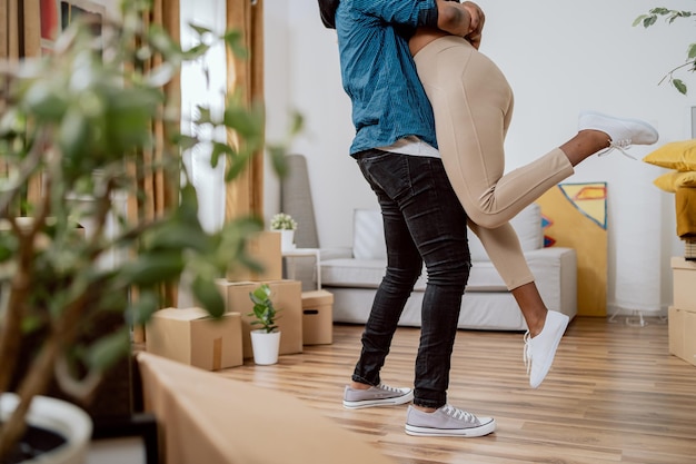 Man hugs his girlfriend wife lifts up with happiness shot of legs in background of apartment with ca