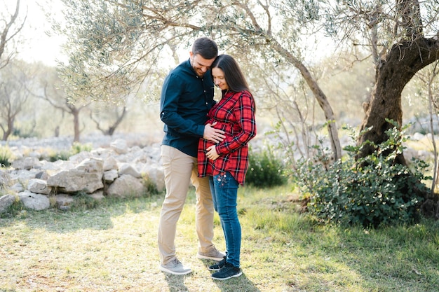 Man hugs pregnant woman in a park near a tree