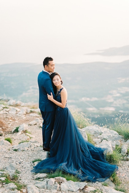 Man hugs woman in a mermaid dress standing on top of a mountain