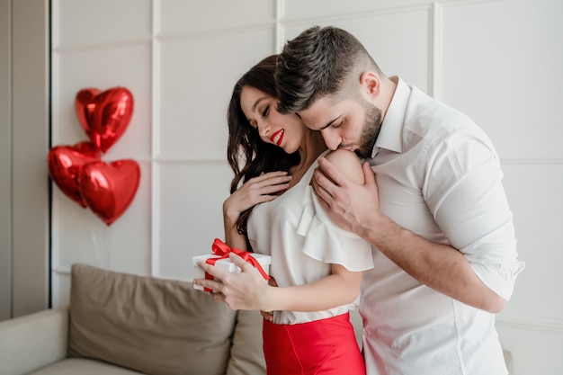 Man hugs woman with present in gift box at home in modern apartment