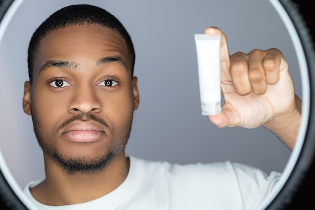Man huidverzorging cosmetisch product reclame gezichtsbehandeling zelfverzekerde Afrikaanse man die witte mo . presenteert