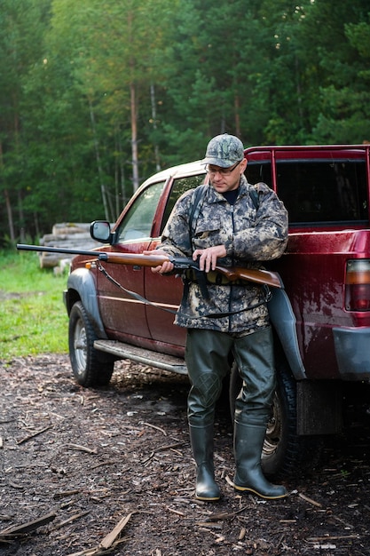 Photo man hunter standing with shotgun rifle near his car outdoor preparing for bird hunt in autumn forest