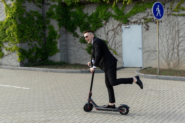 ビジネススーツとサングラスをかけた男が電動スクーターに乗って笑う