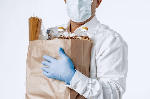 Фото Человек в защитной медицинской маске с сумкой из продуктового магазина
