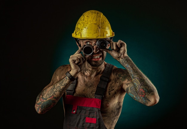 労働者の服を着た男とカメラの鉱夫で裸の体がしかめっ面で煤で汚れたヘルメット