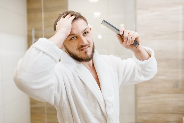 Man in badjas kamt zijn haar in de badkamer