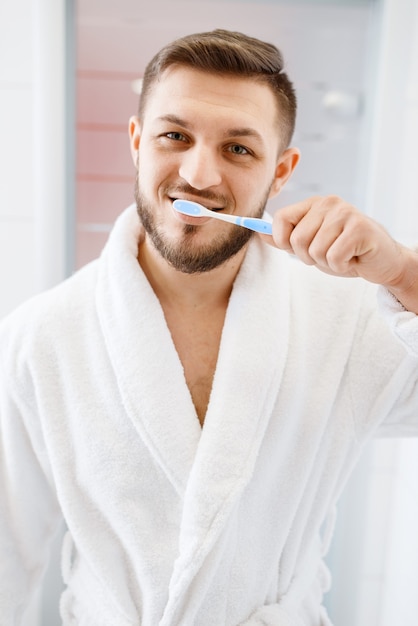 Man in badjas poetst zijn tanden in de badkamer