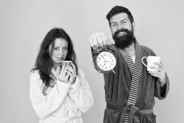 Man in badkleding houdt thee koffie Ontbijtconcept Elke ochtend begint met koffie Paar in badjassen met mokken Het is koffietijd Man met baard en slaperige vrouw geniet van koffie of thee in de ochtend