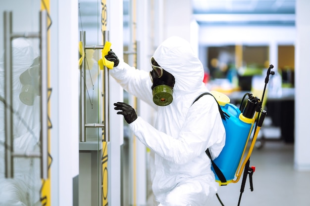 Man in beschermend hazmat-pak wast kantoormeubilair om de verspreiding van coronavirus te voorkomen.