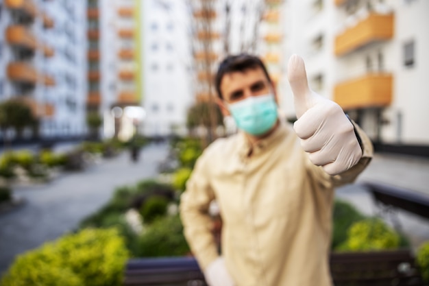 Man in beschermend pak met masker duimen opdagen, event infectie van virus, besmetting van ziektekiemen of bacteriën. Infectiepreventie en bestrijding van epidemieën.