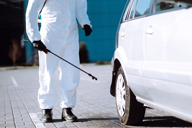 Man in beschermend pak wast en ontsmet autowielen om de verspreiding van het coronavirus te voorkomen