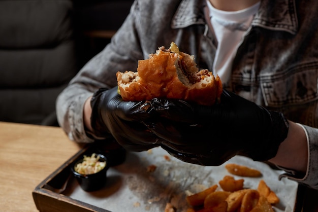 写真 ビーフバーガーのクローズアップを食べる黒い手袋をした男