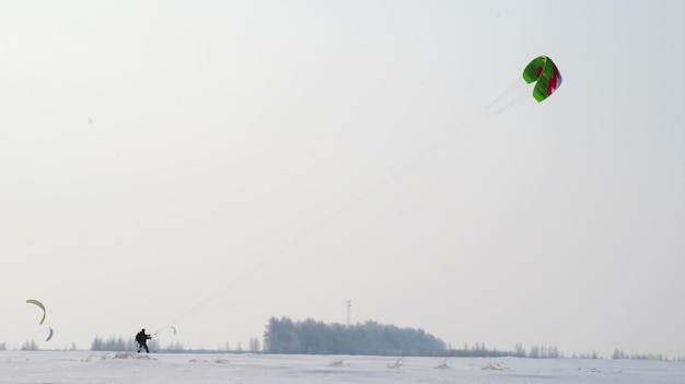 写真 緑の凧を引っ張る黒人の男 フィールドマンはフィールドでスノーカイトをする カイトサーファーは雪の中で風に乗ってパラシュートに乗る
